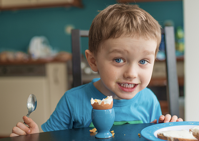 Small happy three year old boy eats an egg